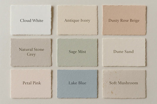 Flatlay of 9 handmade paper swatches for luxury wedding invitations, featuring trending 2025 colors like cloud white, antique ivory, dusty rose beige, natural stone grey, sage mist, dune sand, petal pink, lake blue